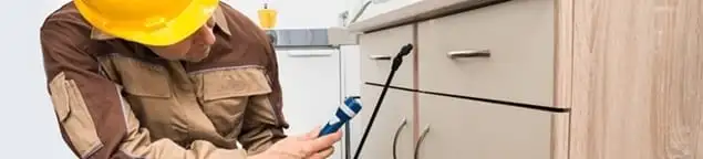 Roach exterminator applying treatment under kitchen cabinets in Chicago, IL